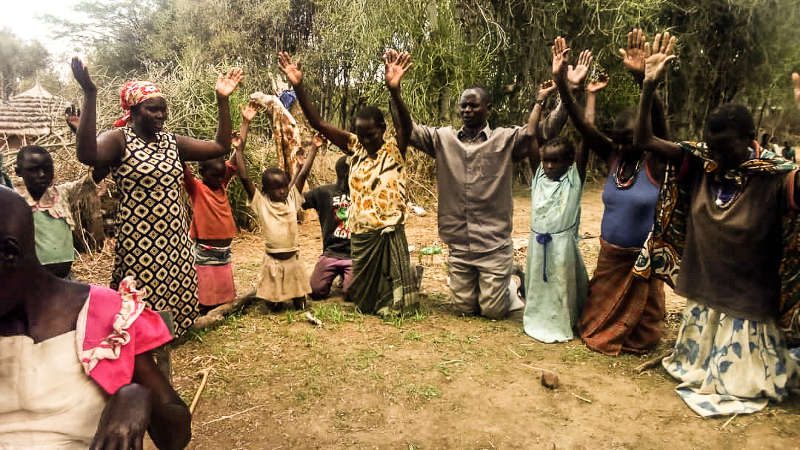 Ugandan Christians on their knees in a circle with their hands lifted praying and praising God