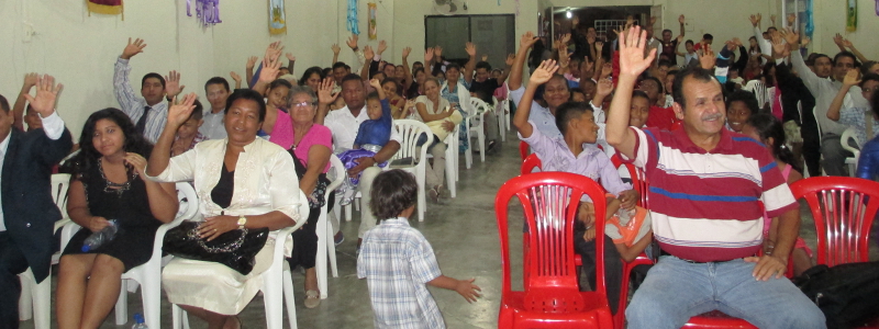 Ecuadorian Christians sitting plastic yard chairs for church and raising their hands