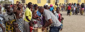 Man pulls essential supplies from a cardboard box to give to a group of Nigerian women and their children