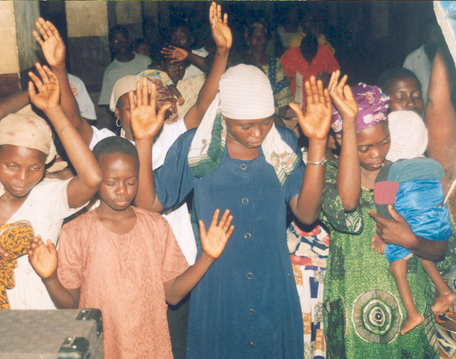A group of Sierra Leonean Christian women holding up their hands while worshiping together