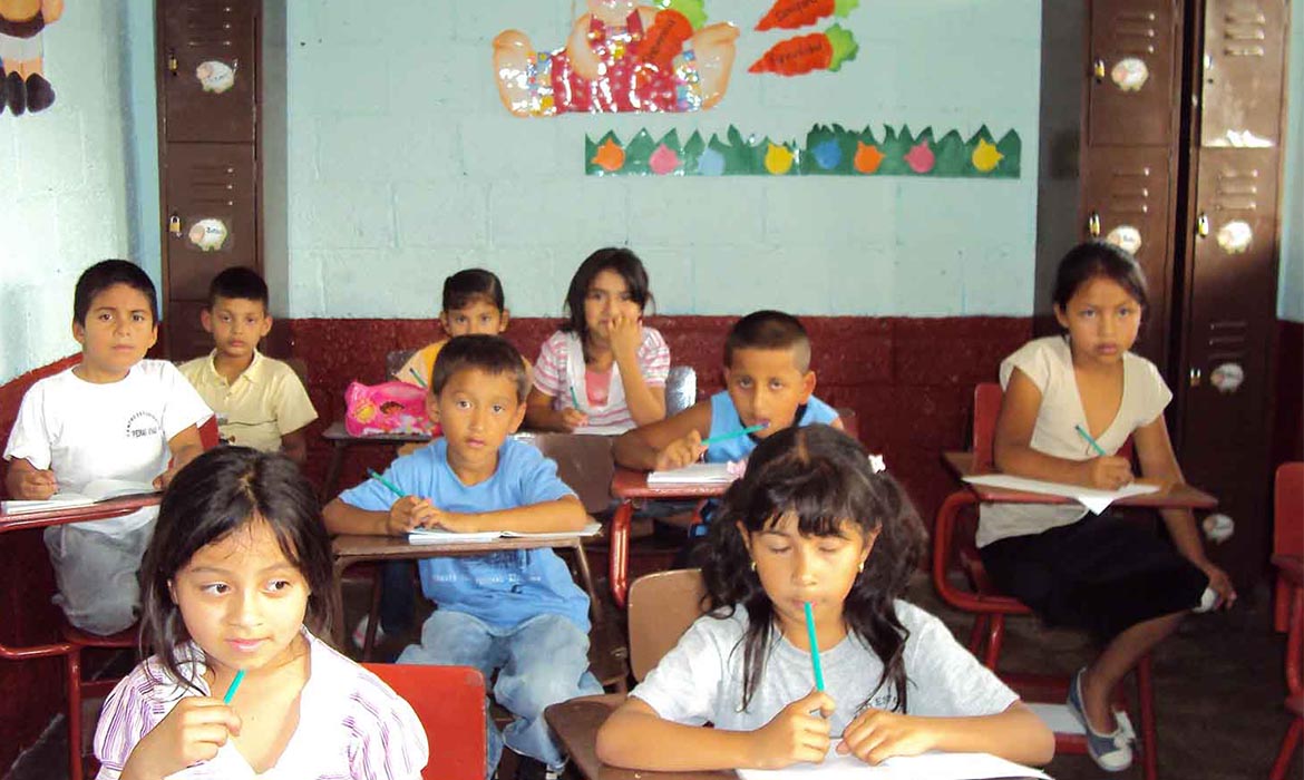 Guatemalan children sit at their desks in school with a notebook and pencil in hand
