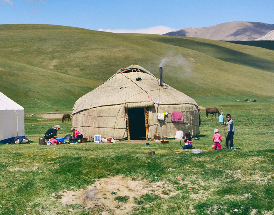 Kyrgyz mother and children working outside of their rawhide house located in a green valley
