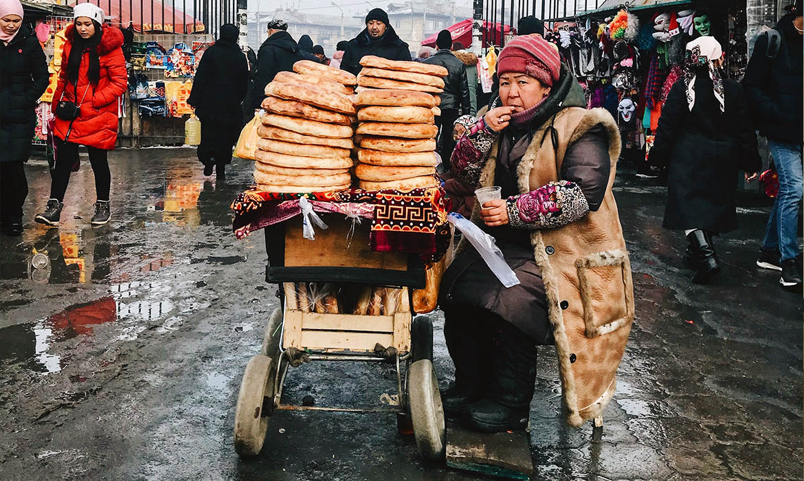 Eurasian woman sitting in a marketplace with a cart full of bread that she is selling