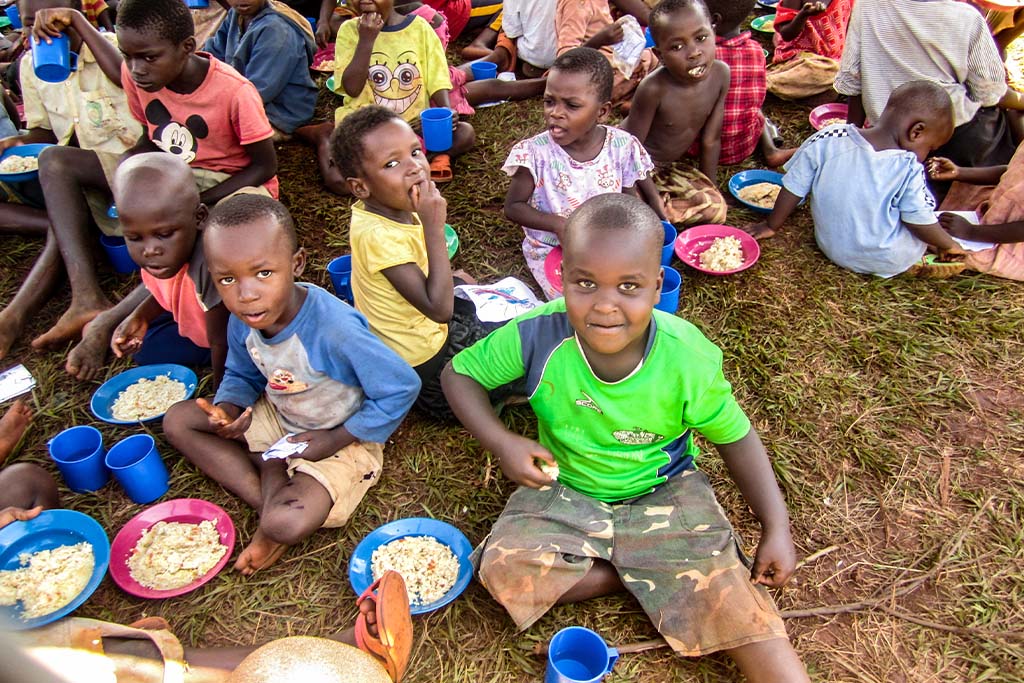 Young Ugandan children sit on the ground eating rice and drinking water