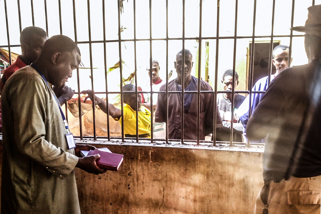 Malian Christian missionary holds a Bible while sharing the gospel with inmates standing behind bars