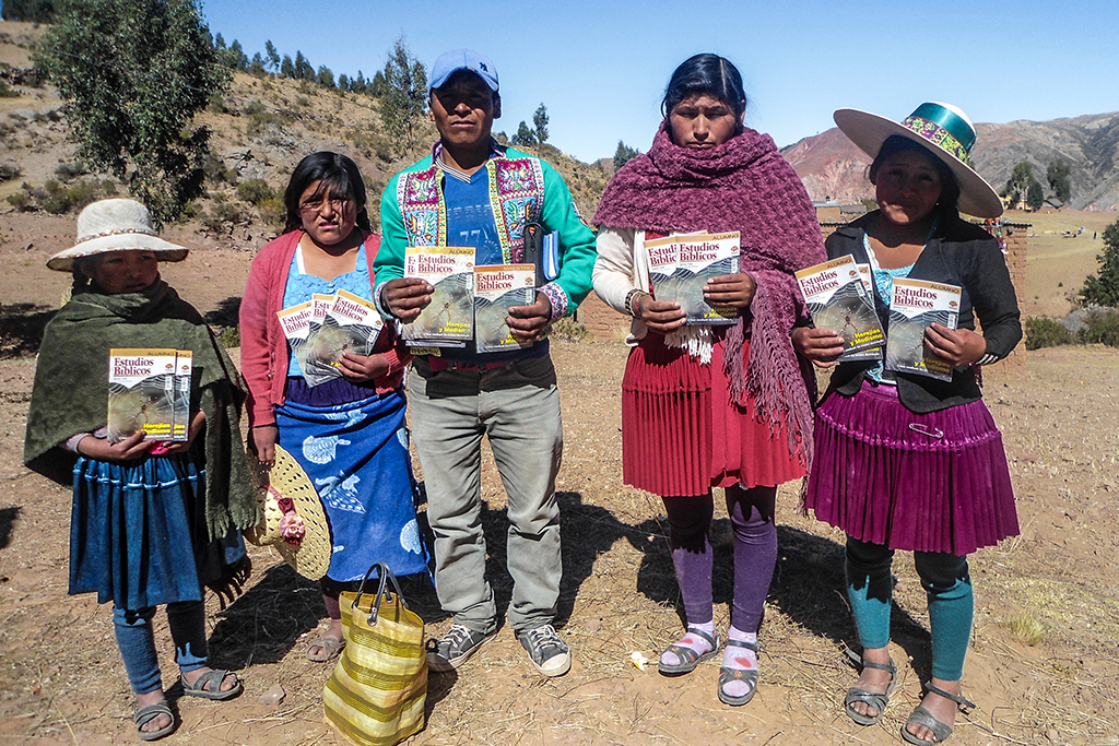 Bolivian man and his wife and three daughters stand in a dry valley holding up their Bible study books