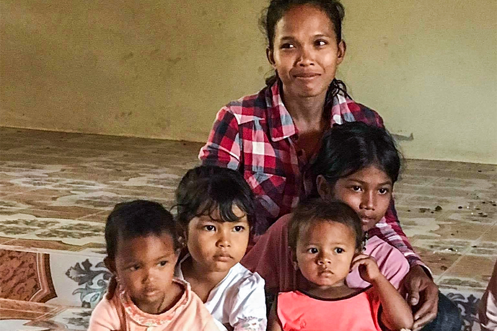 Cambodian woman sitting on the floor of her house with her four young girls