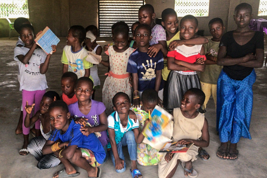 Ghanaian school children stand together in their school some holding notebooks and coloring books