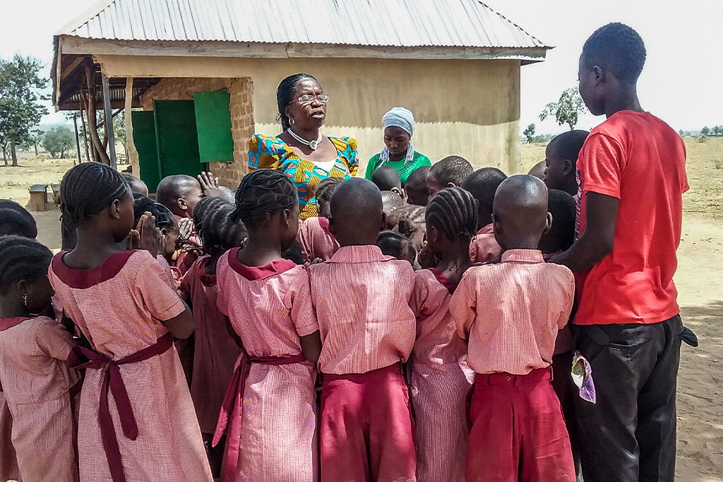 Nigerian school children stand around their teacher in their red uniforms praying to the Lord