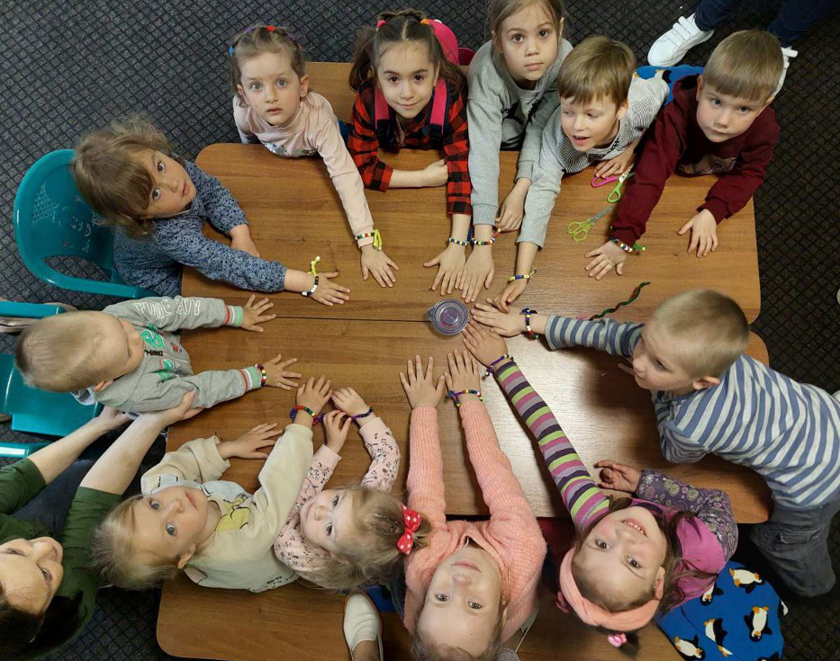 Slovakian children sitting at wooden table each with a hand reaching toward the middle