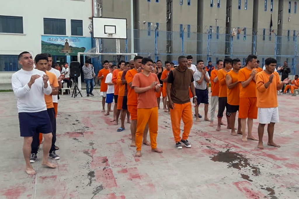 Ecuadorian inmates wearing orange stand in lines clapping their hands while listening to music