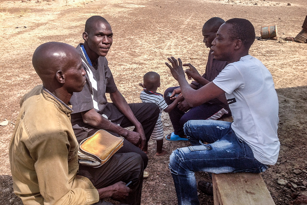 Burkinabé Christian men sit outside on wooden benches discussing the Bible
