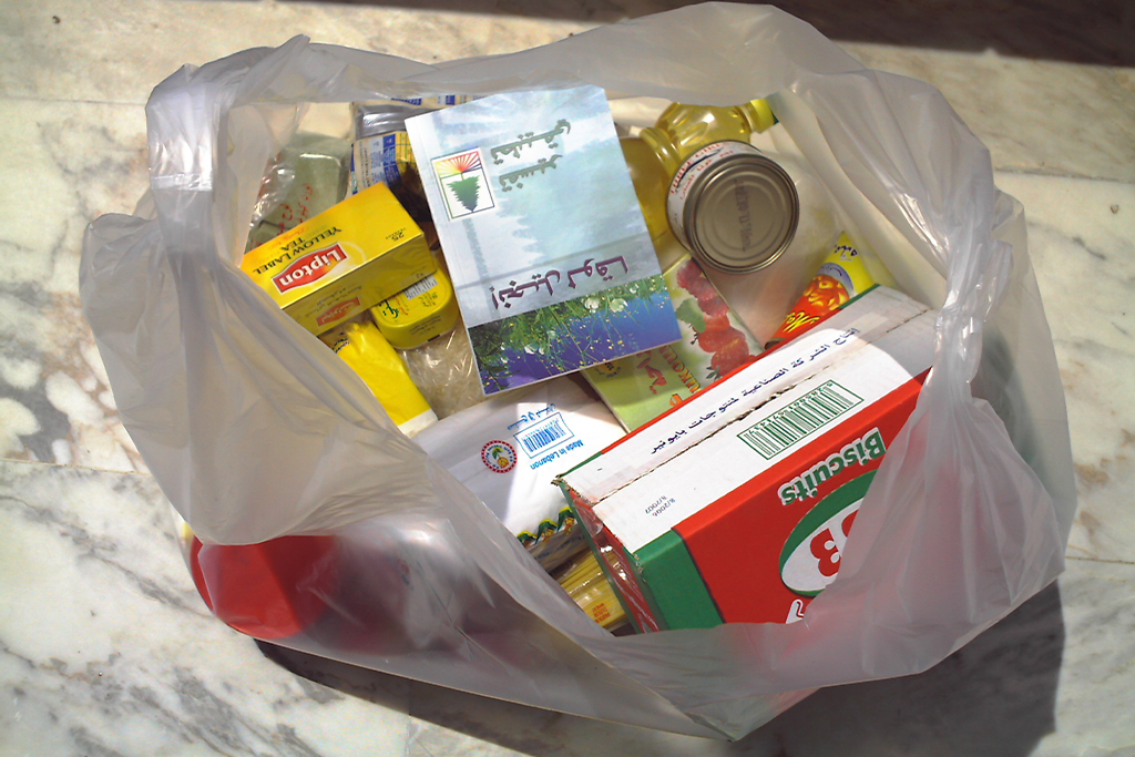 A bag of groceries filled with tea, oil, and canned goods