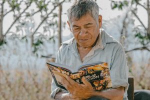 Mexican man sits outside in chair reading a Christian action bible.