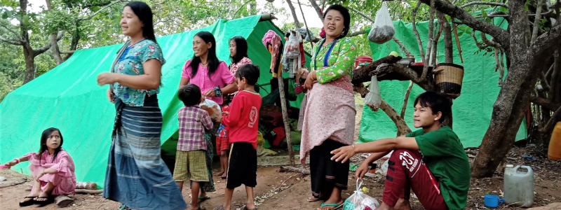 Women and children gathering outside of two tents made from green tarps