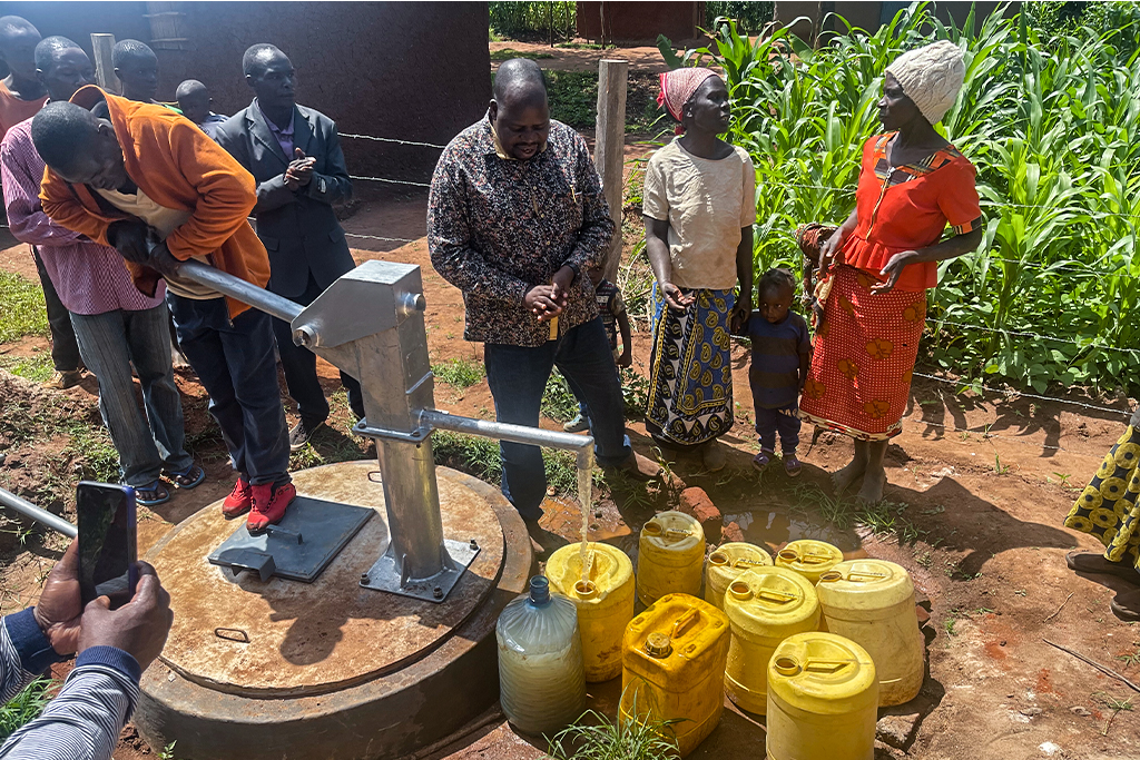 A group of Kenyan people pump water from a community well into yellow jugs