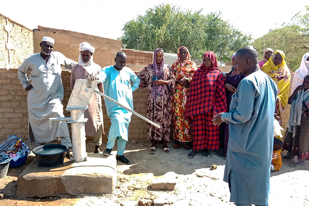 Chadian men and women stand around their town well to pump water