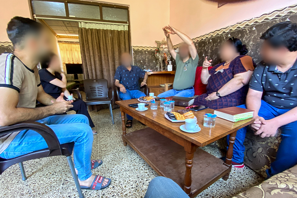 Iraqi Christians sit in chairs and on couches for a bible study.