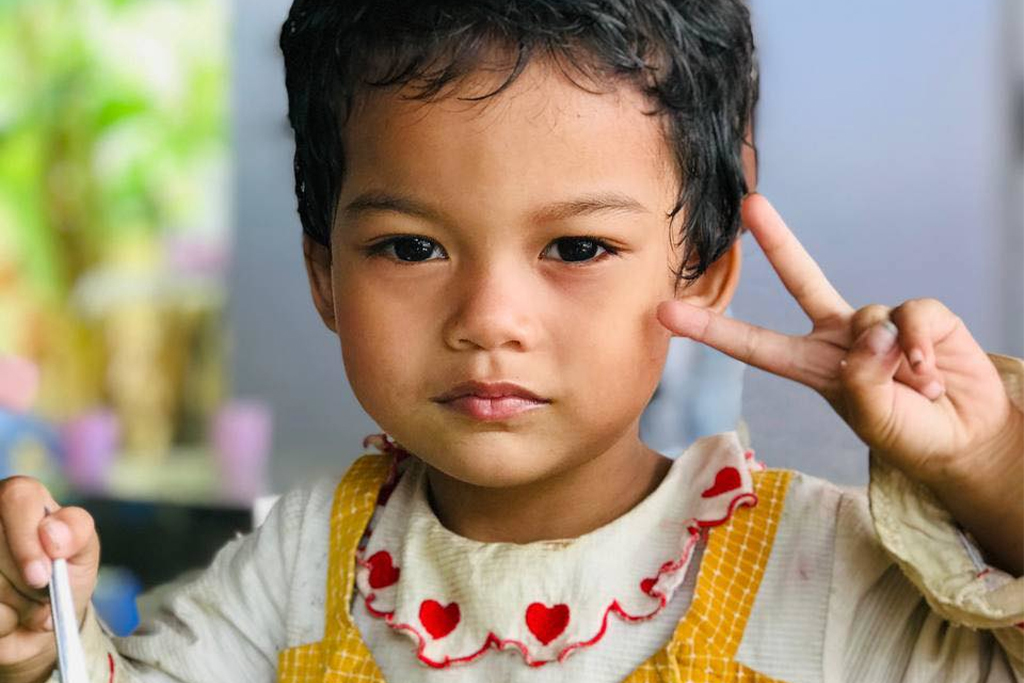 Little Burmese boy holding a spoon while making a peace sign