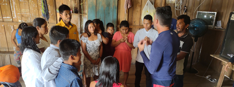 Brazilian Christian missionary prays with men and women in wooden house