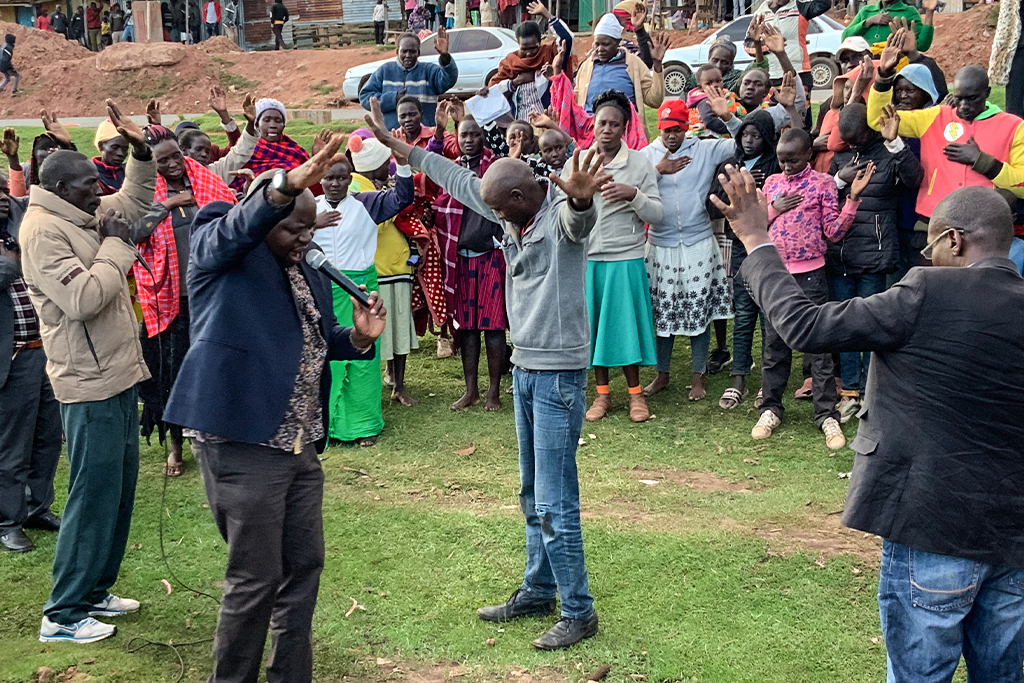 Kenyan Christians gather in a circle outside praising God with their hands raised