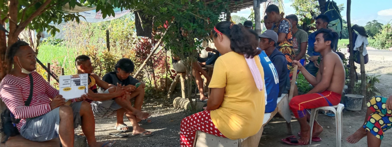 Christian missionary explaining the Gospel using a picture to a group of Filipino men and women under a tree