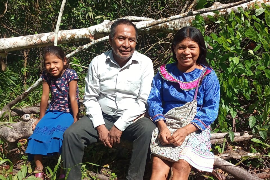 Peruvian husband and wife sit with their daughter on a fallen tree