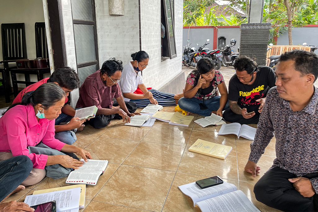Indonesian Christians sitting outside on a tan tile floor intently studying the Bible