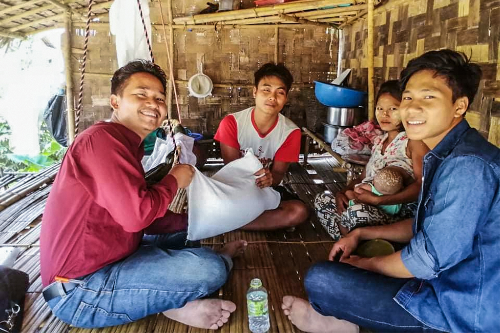 Burmese family sitting in their shelter made from bamboo two of them holding a sack of food