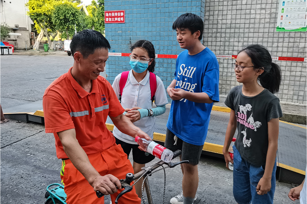 Chinese man wearing orange sitting on a bike talking to teenagers