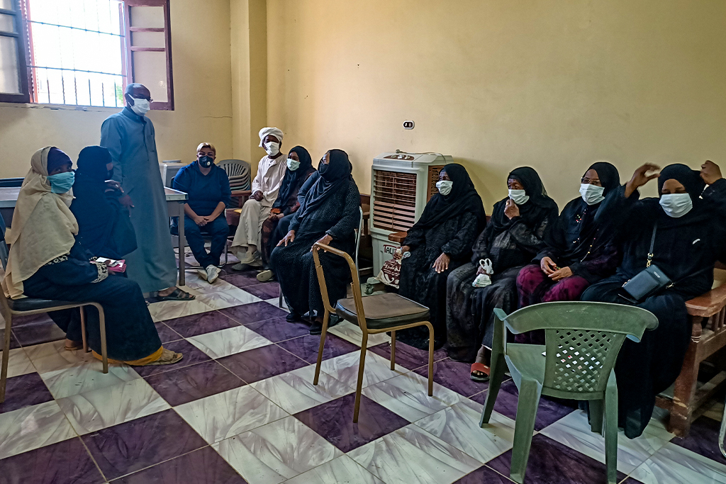 African women sitting in chairs wearing head coverings and masks