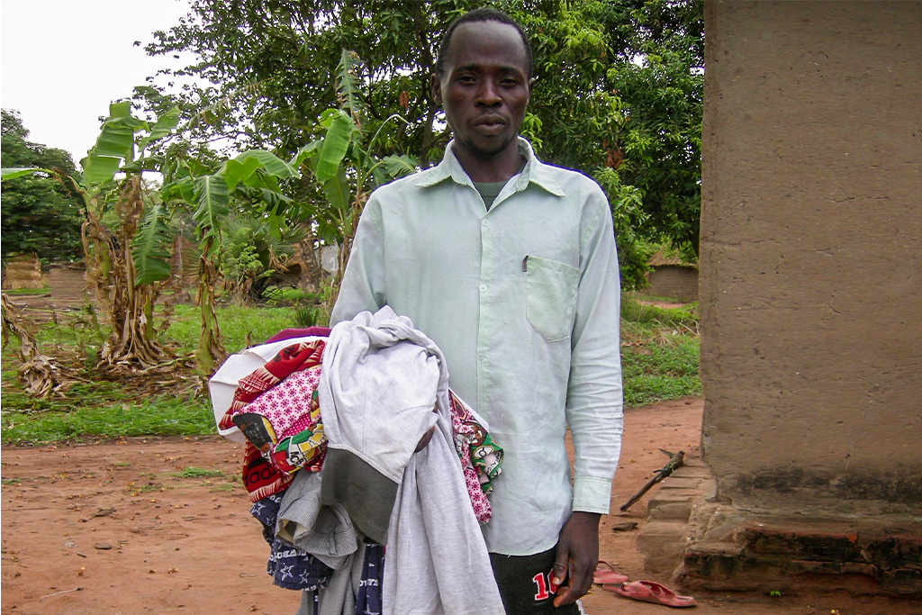 Cameroonian Christian missionary standing outside holding a bundle of clothes in his right arm
