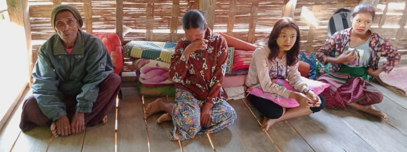 A Burmese family sitting on a wooden floor with blankets behind them