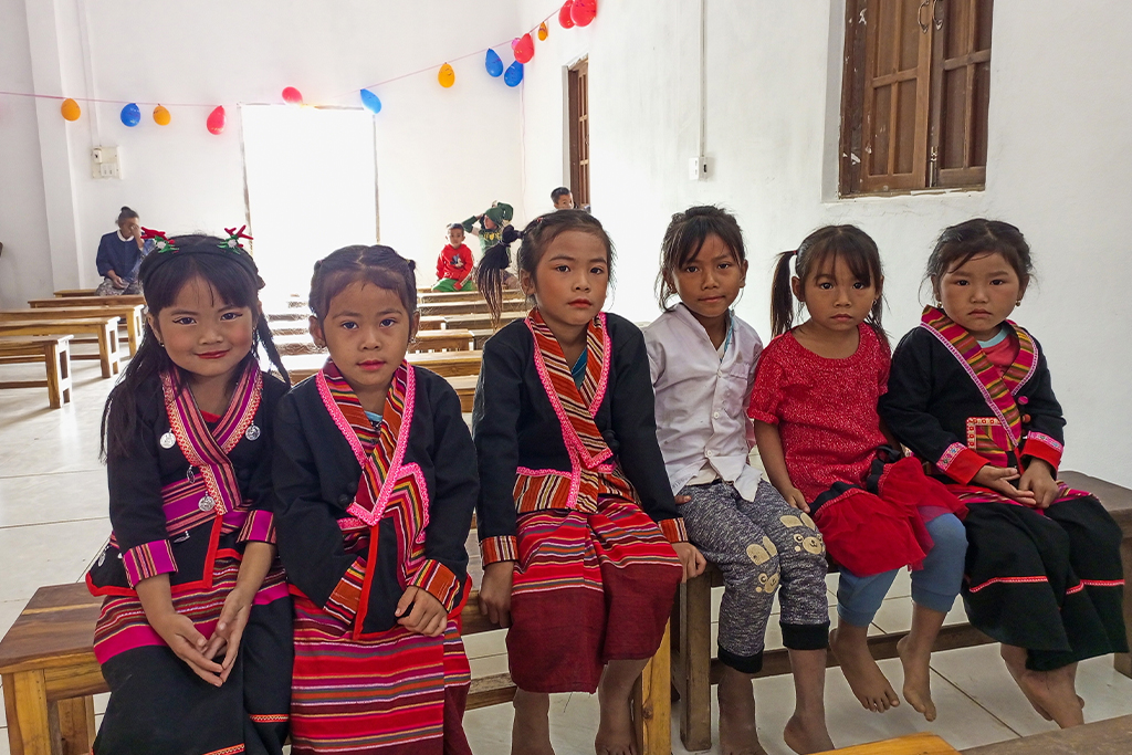 Laotian children, most of them wearing uniforms, sitting on wooden benches in a church
