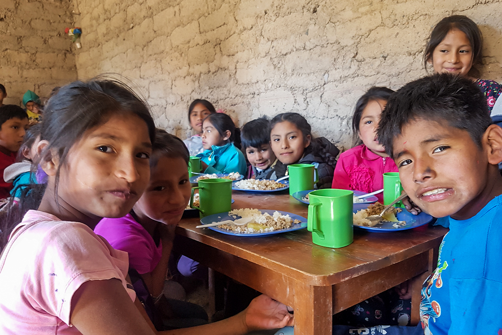 Peruvian children eating rice and ground beef in a feeding center made of clay bricks and mud