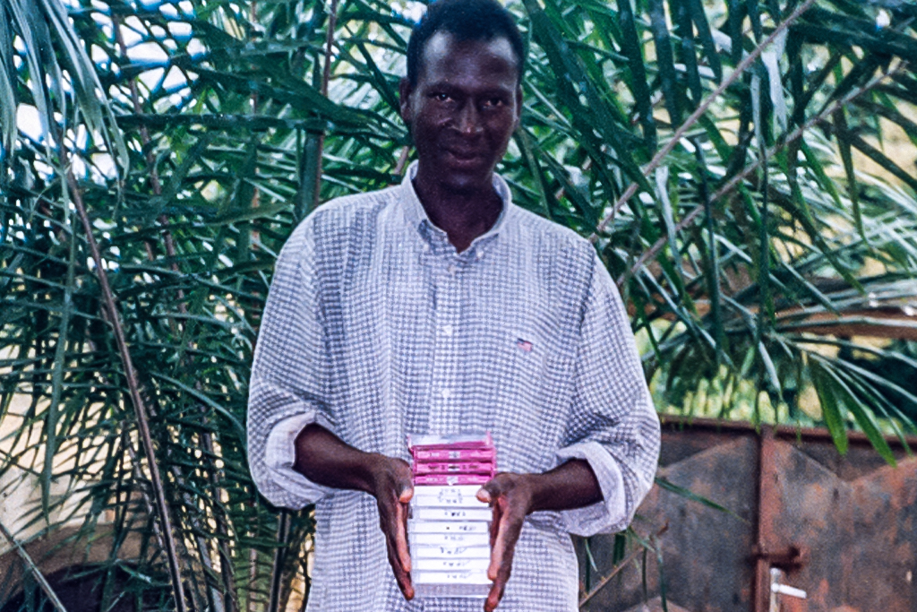 Togolese Christian evangelist standing in front of a bush holding a stack of tapes for teaching