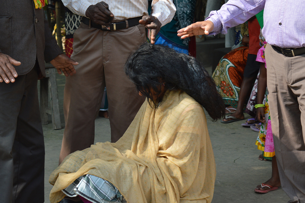 A South Asian woman sits on the ground while three South Asian pastors stretch out their hands and pray for her.