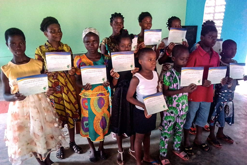 School children in Gambia hold up certificates for the classes they have completed.