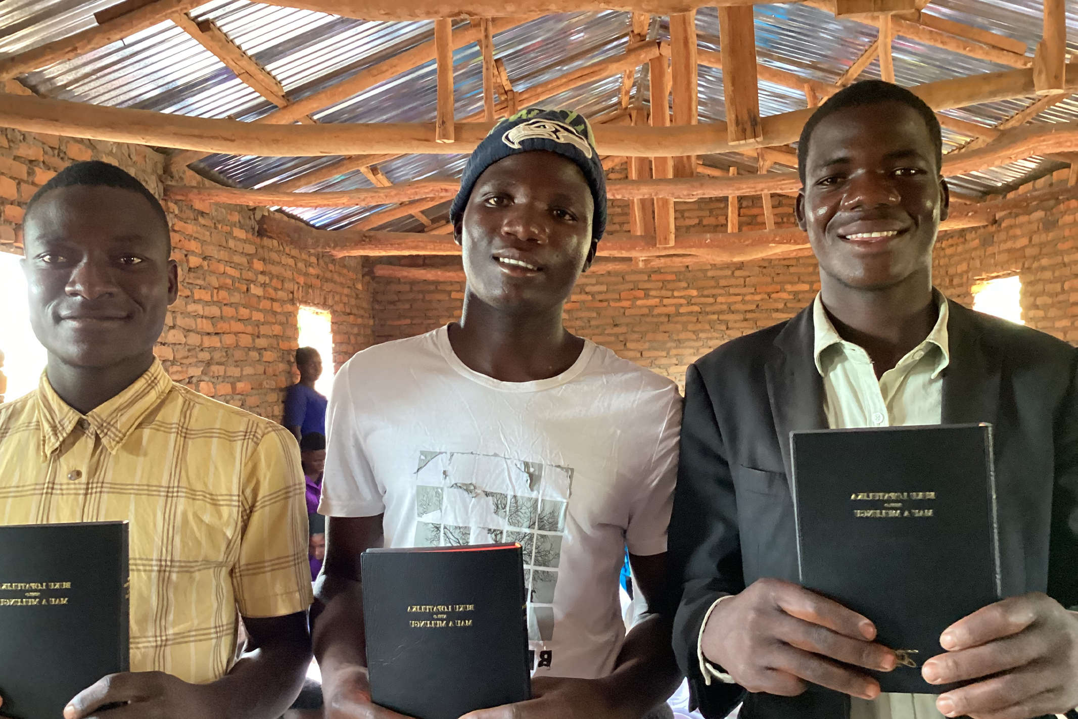 Teenage Christians in Malawi holding their Bibles while standing in their church which is made of clay bricks and a tin roof