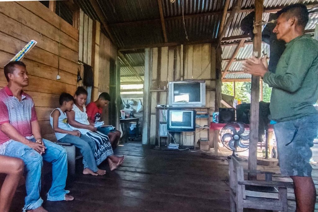 Brazilian man standing in front of others leading a bible study in a home with a tin roof