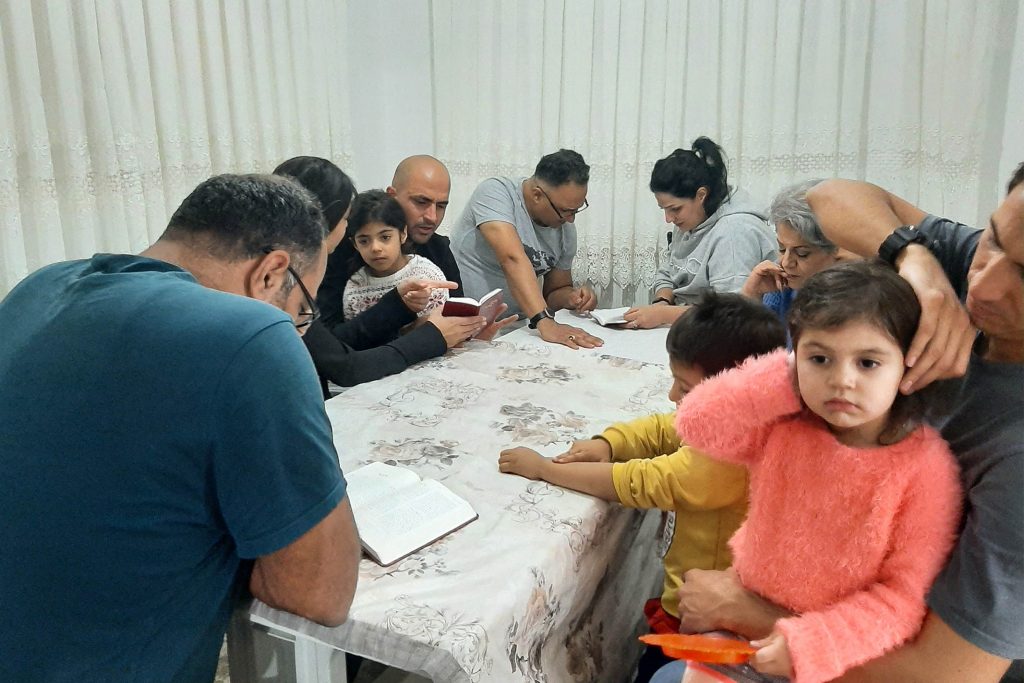 Turkish Christians sitting around a table in a small room with their children for a Bible study