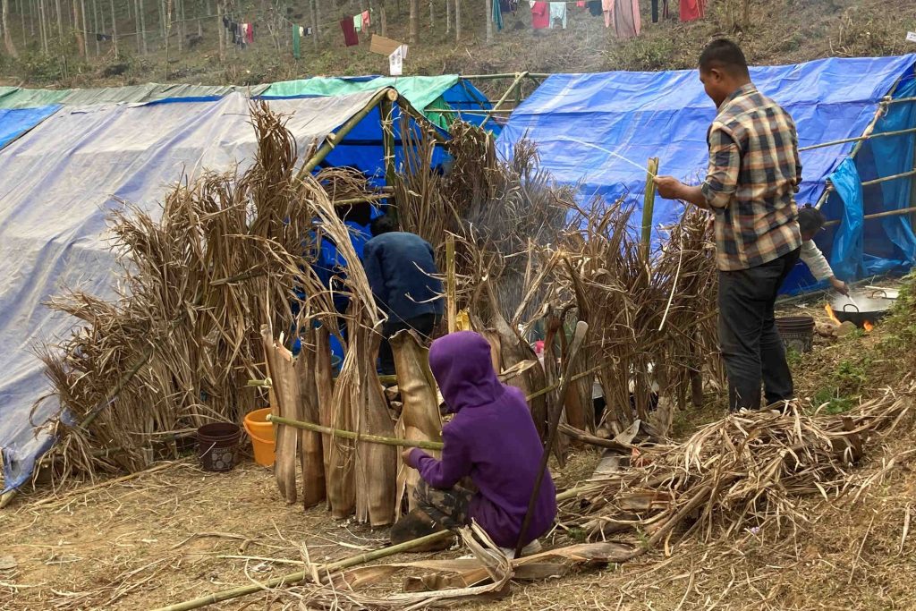 South Asian man and children using dried grasses to make a wall for their shelter