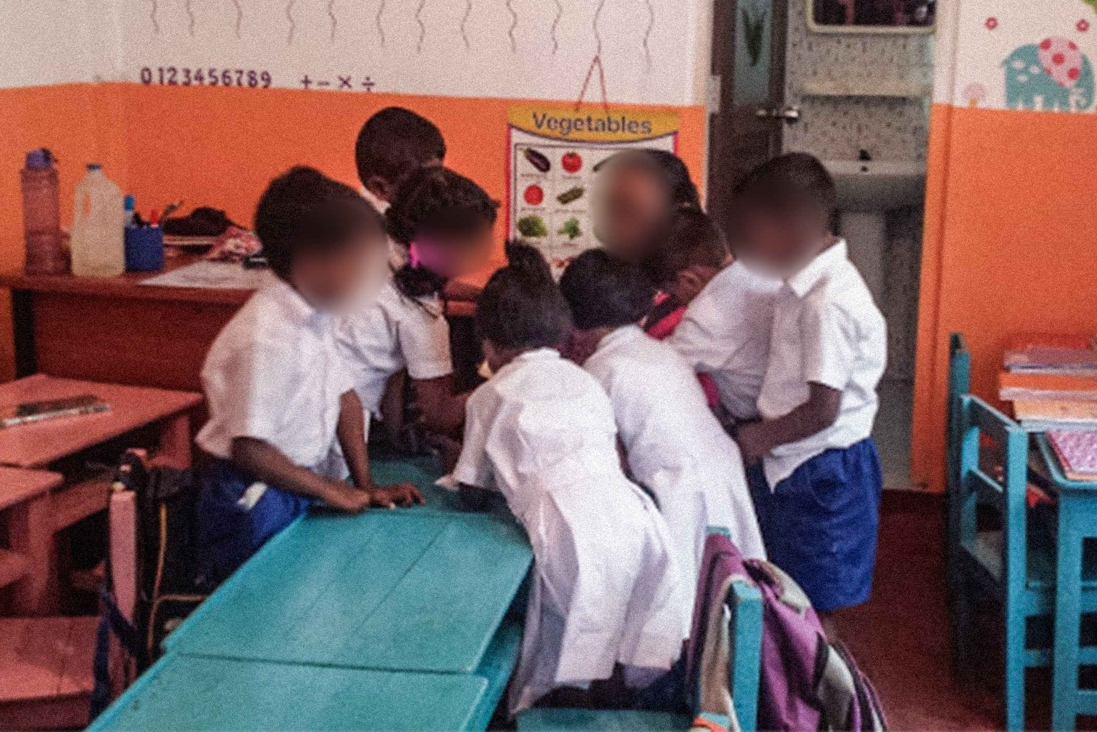 Sri Lankan children wearing their white and blue uniforms at school crowding around their teacher