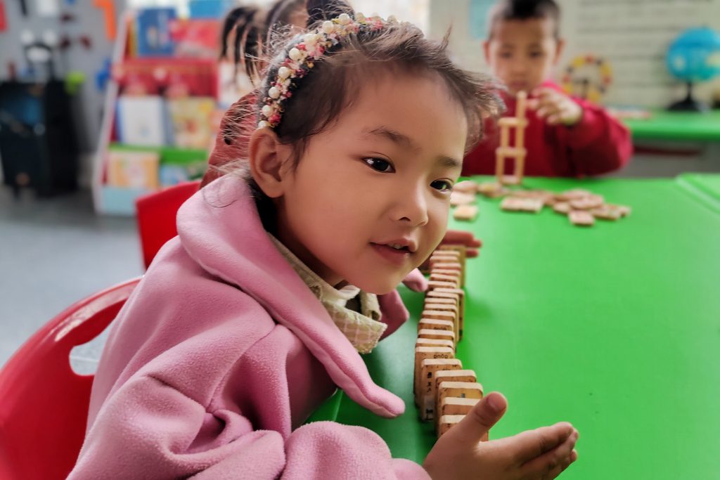 Chinese children sitting in red chairs playing with dominoes at a green table