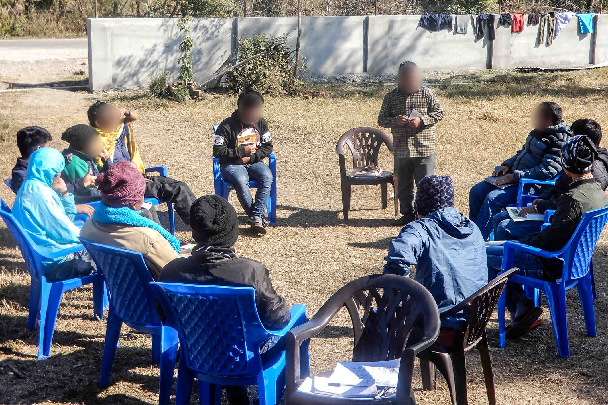 Nepalese Christians meeting outside wearing warm clothes sitting in blue lawn chairs for a Bible study