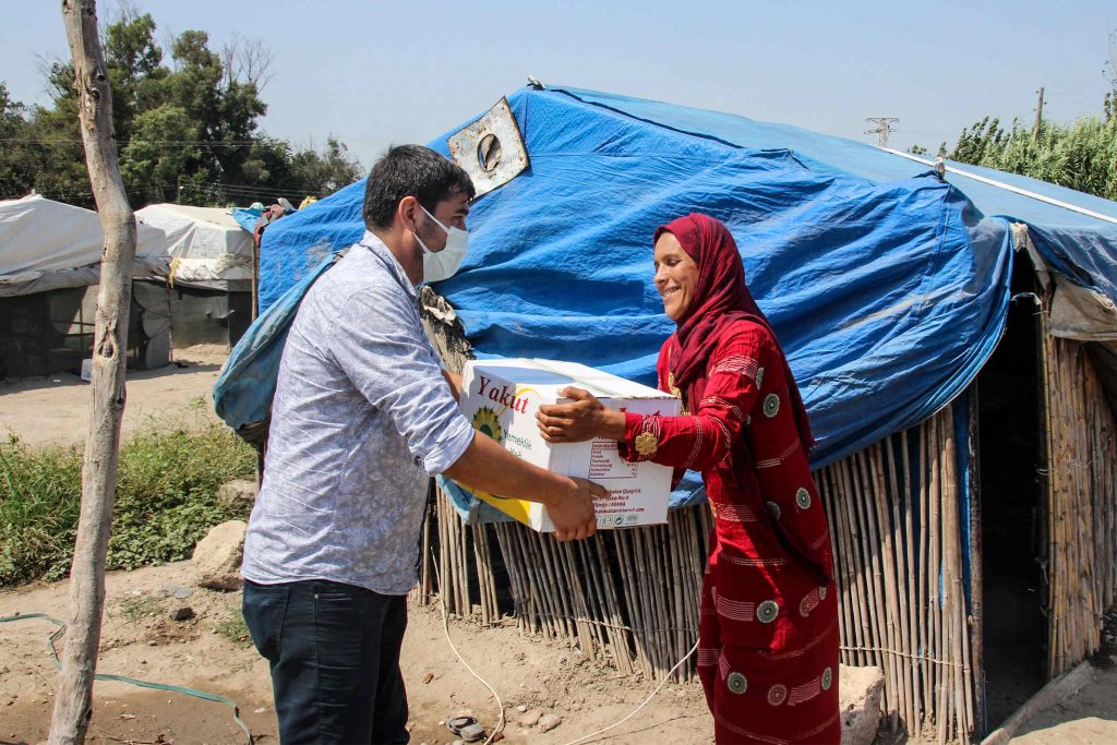 Christian missionary delivers food to a Middle Eastern woman wearing a red head covering in a refugee camp