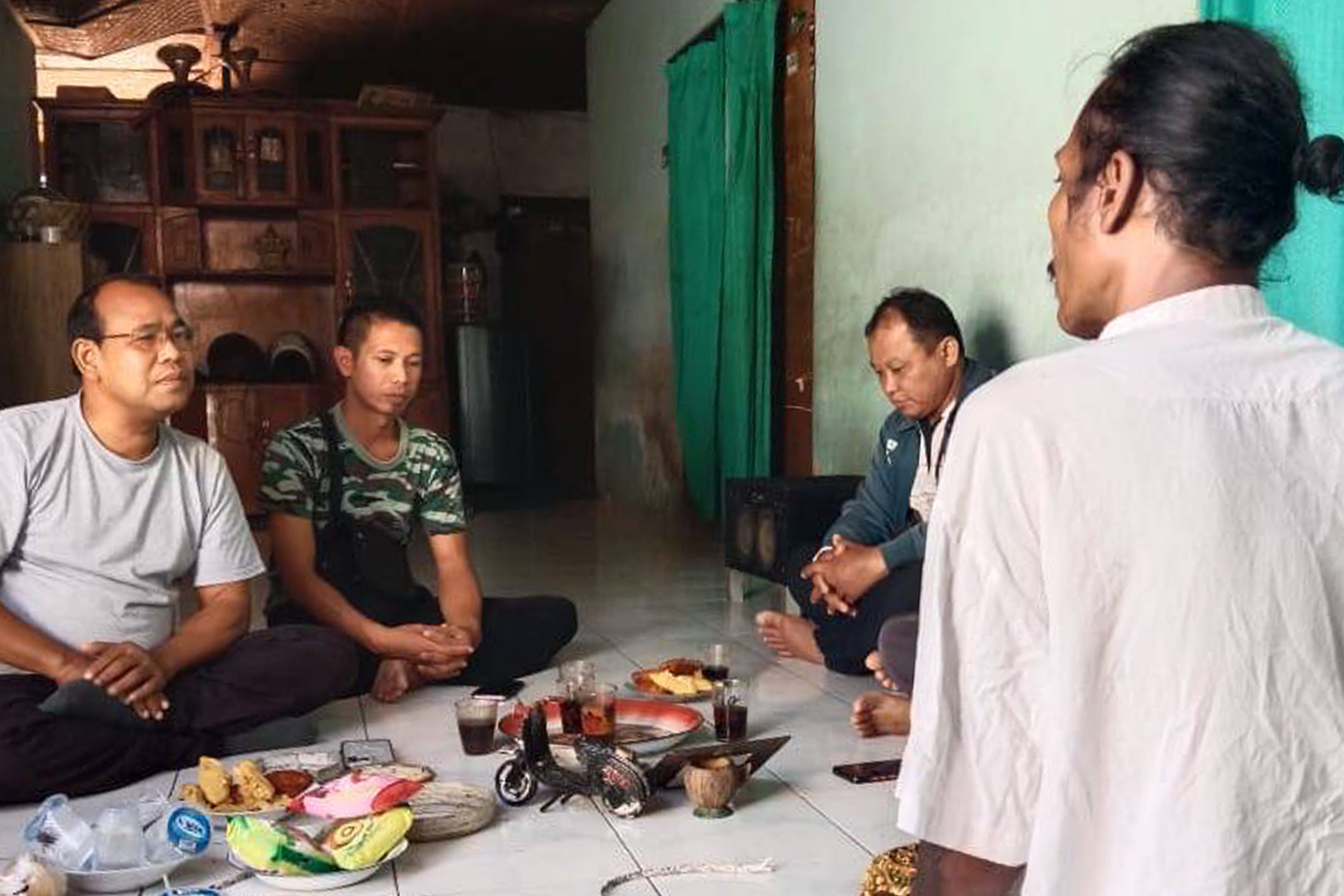 Indonesian men sitting cross-legged on the floor sharing a meal together