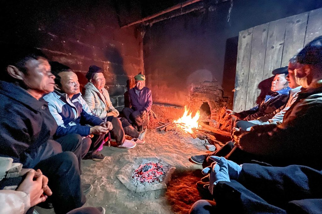 Chinese men and women sitting around a fire in a house made of cinder blocks