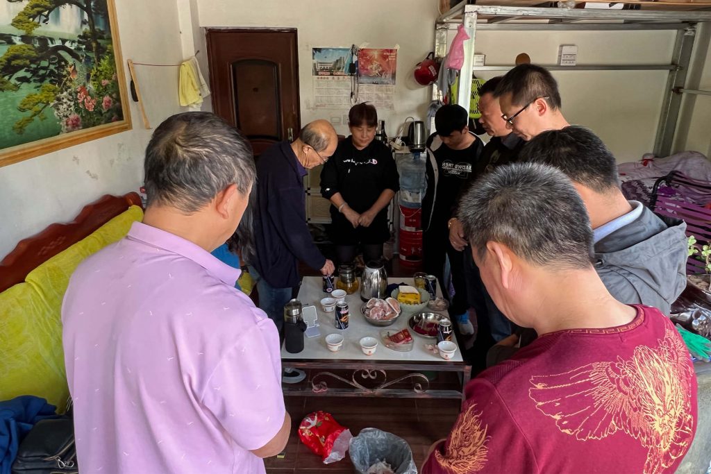 Christians in China stand around a coffee table praying before they eat together