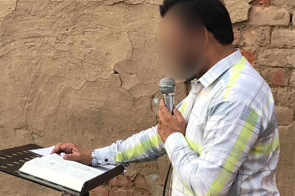 Pakistan Christian pastor preacher while holding microphone and standing next to a brick wall